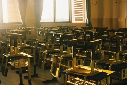 Sala de aula vazia, iluminada pelo sol, com cadeiras empilhadas sobre as mesas.