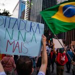 Manifestantes participam de ato em São Paulo, no Brasil, segurando cartazes sobre direitos humanos e democracia.