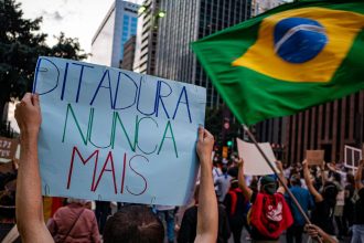 Manifestantes participam de ato em São Paulo, no Brasil, segurando cartazes sobre direitos humanos e democracia.
