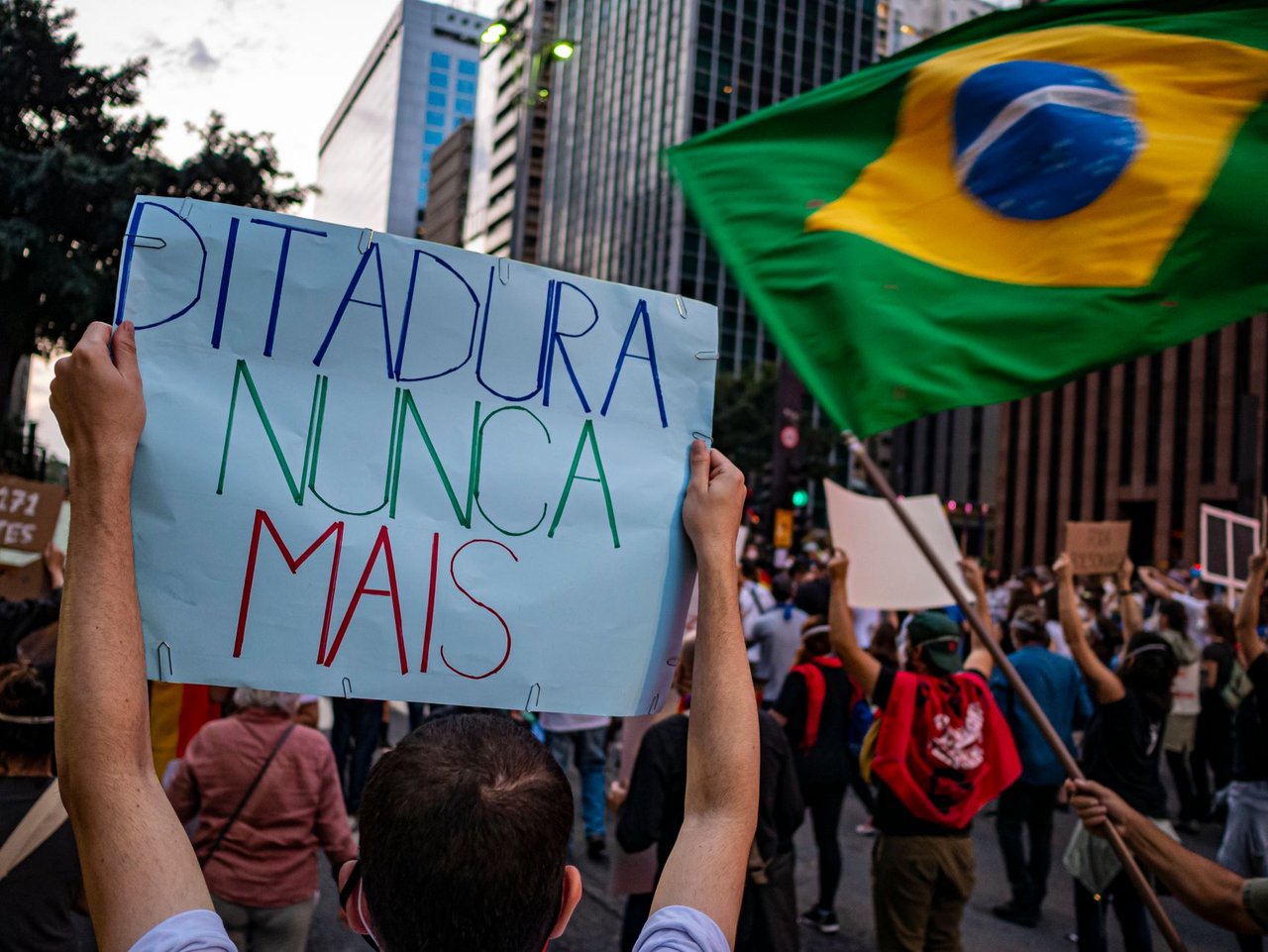Manifestantes participam de ato em São Paulo, no Brasil, segurando cartazes sobre direitos humanos e democracia.