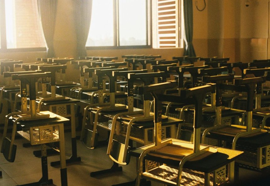 Sala de aula vazia, iluminada pelo sol, com cadeiras empilhadas sobre as mesas.