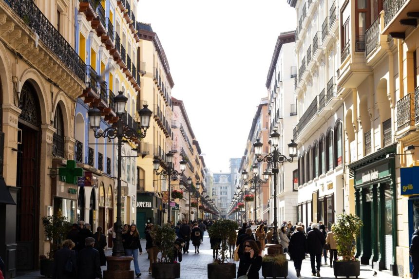 Rua movimentada de Zaragoza, na Espanha, com pedestres circulando entre edifícios urbanos.